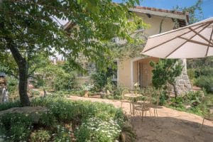 Well-maintained house with a green tree and landscaped patio yard, featuring an outdoor dining table, chairs, and a sun umbrella.