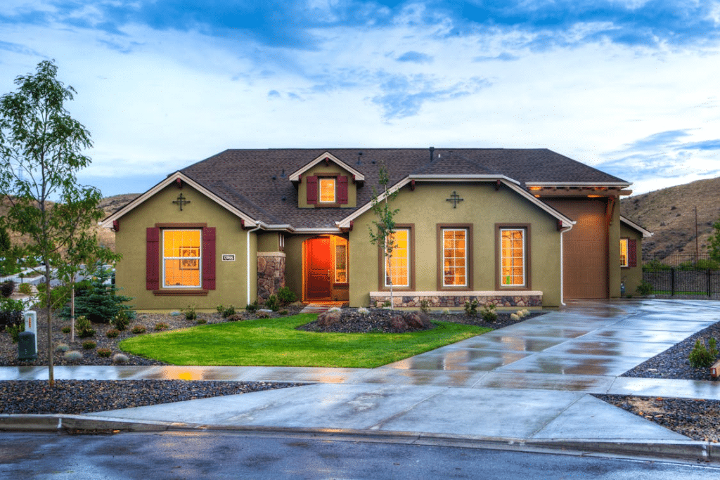 Clean green house with a freshly pressure-washed garage floor and sidewalk, neatly trimmed plants, and well-maintained mulch beds, highlighting a polished, cared-for exterior.