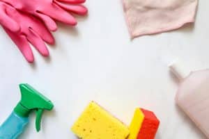 Cleaning supplies including gloves, sponges, a spray bottle, and a cloth arranged on a white surface, representing tools for exploring the question: Is Bleach or Vinegar Better for Cleaning Concrete?